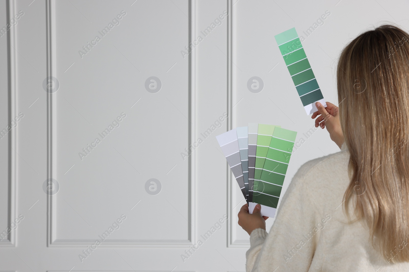 Photo of Woman choosing color for wall indoors, focus on hands with paint chips. Interior design