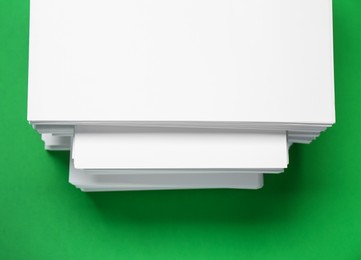 Stack of white paper on green background, top view