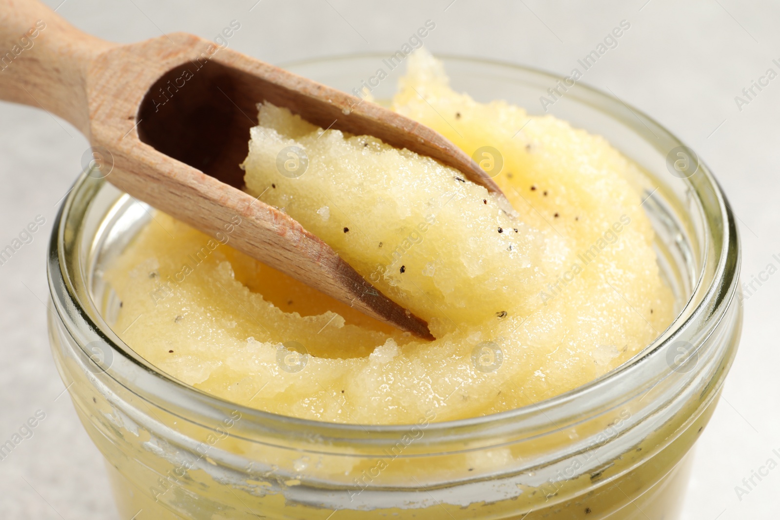 Photo of Body scrub with scoop in glass jar on light grey background, closeup