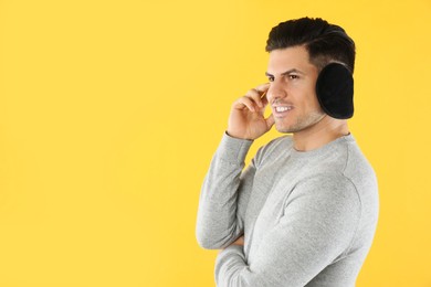 Man wearing stylish earmuffs on yellow background. Space for text