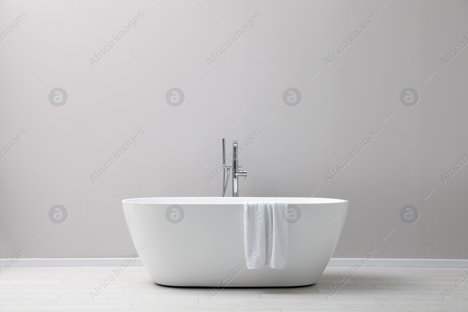 Photo of Modern ceramic bathtub with towel near light wall indoors