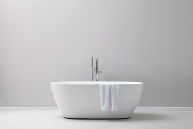 Modern ceramic bathtub with towel near light wall indoors