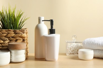 Different bath accessories and houseplant on wooden table against beige background, closeup
