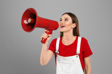 Young woman with megaphone on light grey background