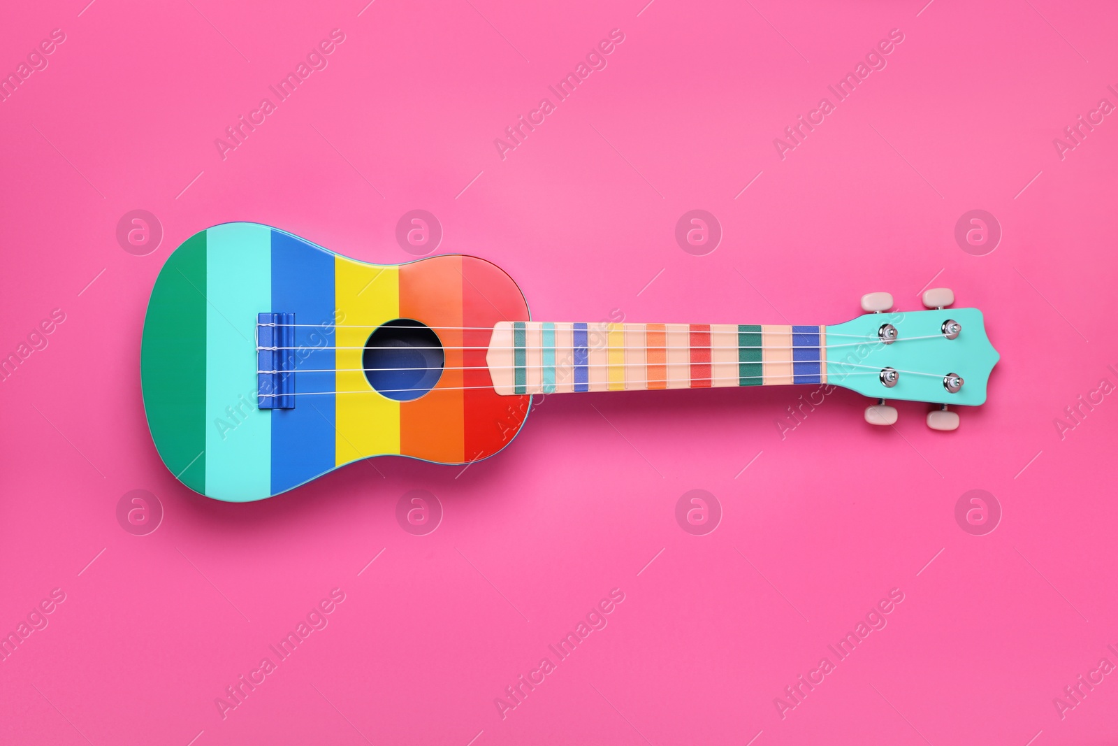 Photo of Colorful ukulele on pink background, top view. String musical instrument