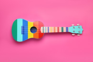 Colorful ukulele on pink background, top view. String musical instrument