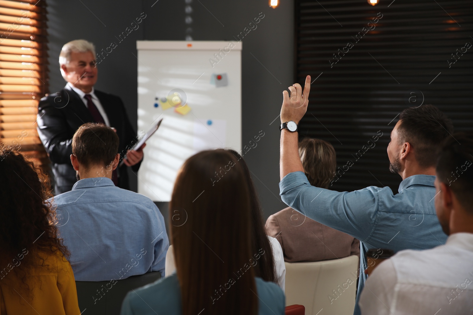 Photo of Man raising hand to ask question at seminar in office