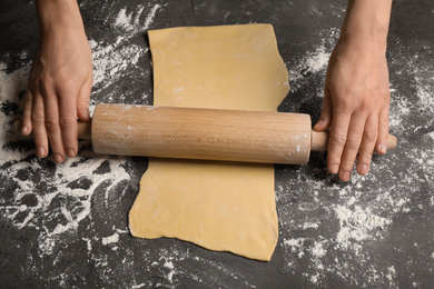 Photo of Woman rolling dough for pasta at grey table, top view