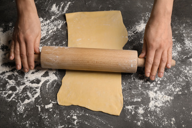 Woman rolling dough for pasta at grey table, top view