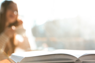 Photo of Book on table in cafe and woman with headphones on background. Audiobook concept