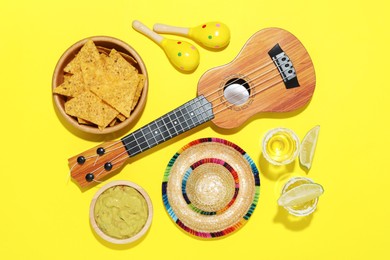 Photo of Mexican sombrero hat, ukulele, tequila, nachos chips, guacamole and maracas on yellow background, flat lay