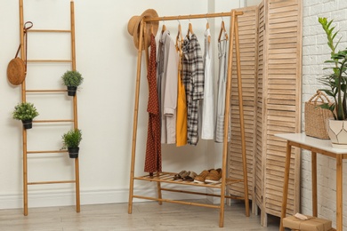 Photo of Stylish wooden table and rack with clothes in modern room interior