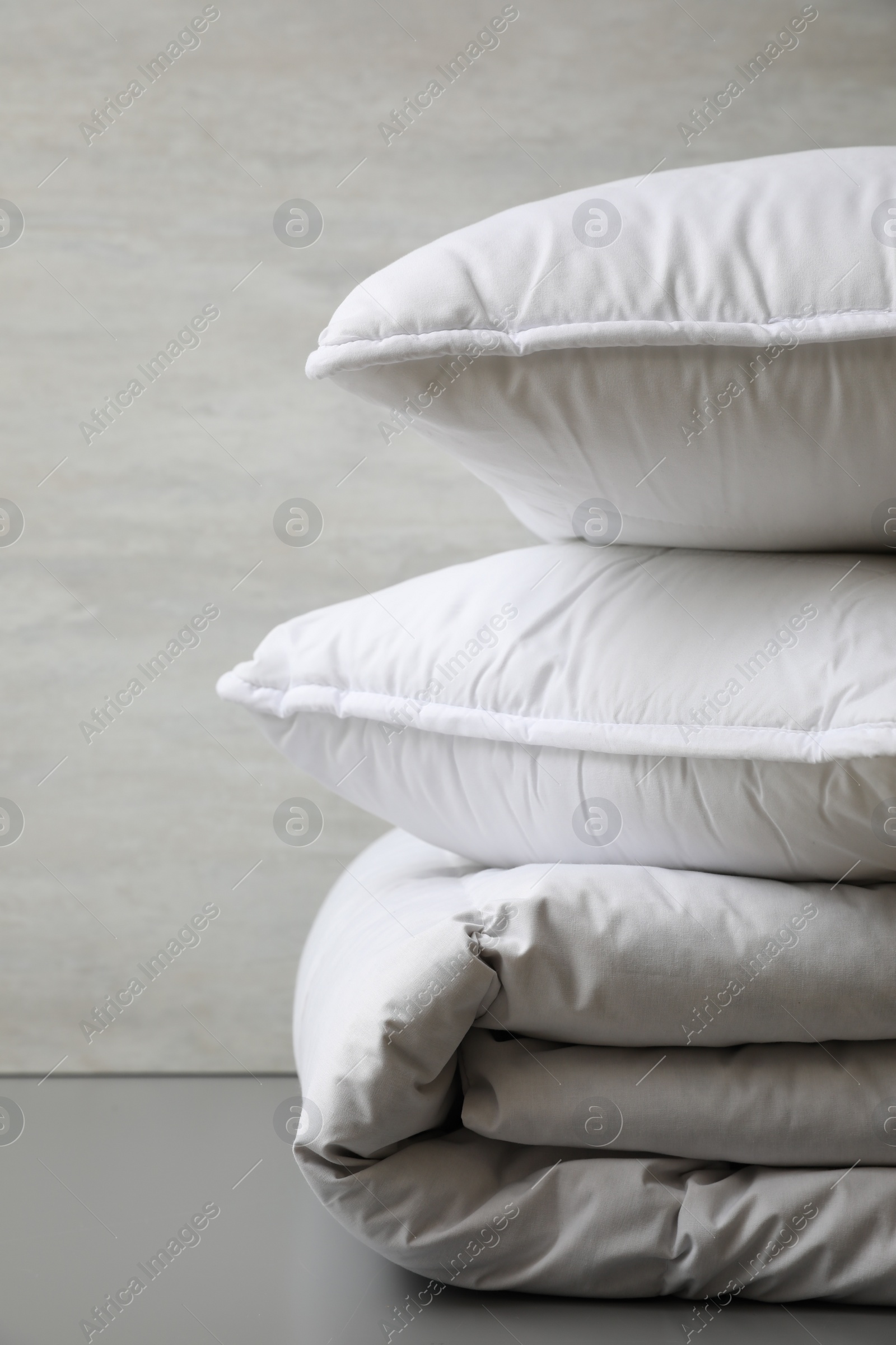 Photo of Soft folded blanket and pillows on light grey table, closeup