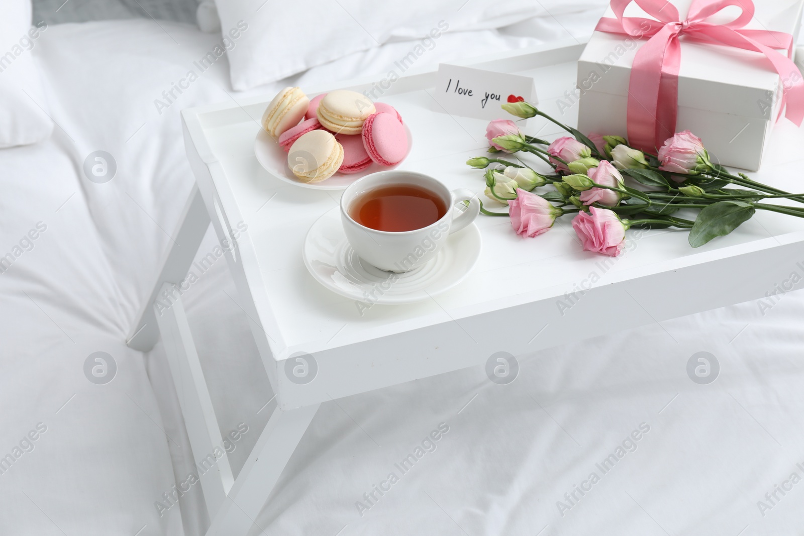 Photo of Tasty breakfast served in bed. Delicious macarons, tea, gift box, flowers and I Love You card on tray