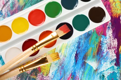 Photo of Watercolor palette and brushes on abstract colorful paint, flat lay