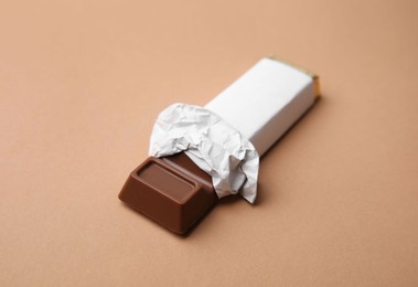 Photo of Tasty chocolate bar in package on light brown background