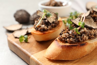 Photo of Tasty bruschettas with truffle paste on wooden board, closeup