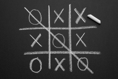 Photo of Tic tac toe game and piece of chalk on blackboard, top view