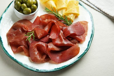 Photo of Delicious bresaola, cheese, olives and rosemary on light textured table