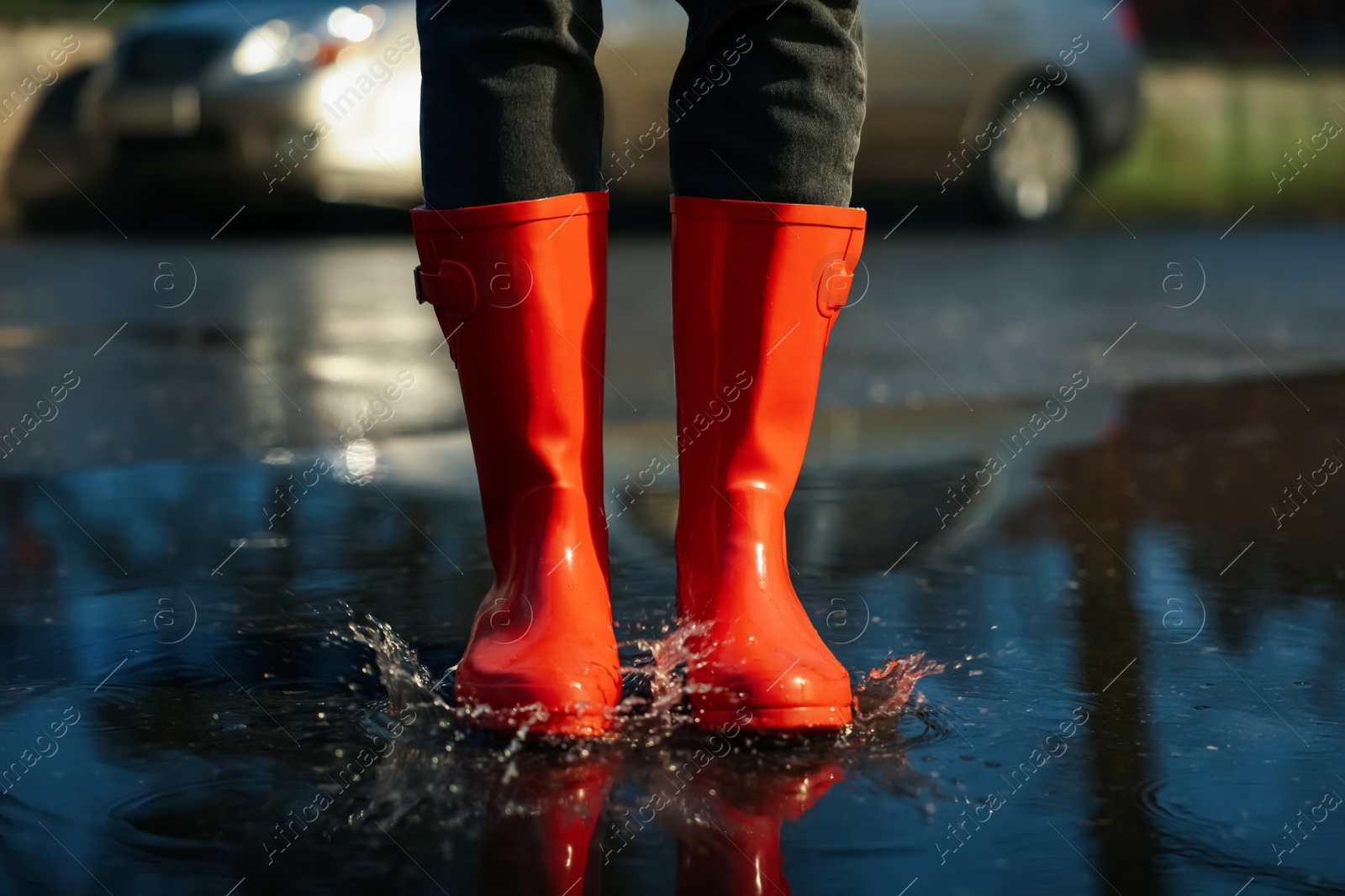 Photo of Woman with red rubber boots in puddle, closeup. Rainy weather