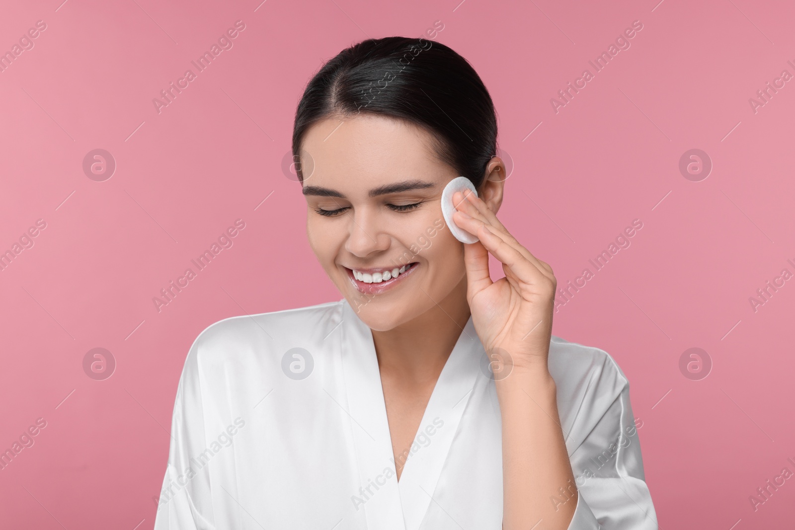 Photo of Young woman cleaning her face with cotton pad on pink background