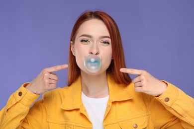 Photo of Beautiful woman blowing bubble gum on purple background