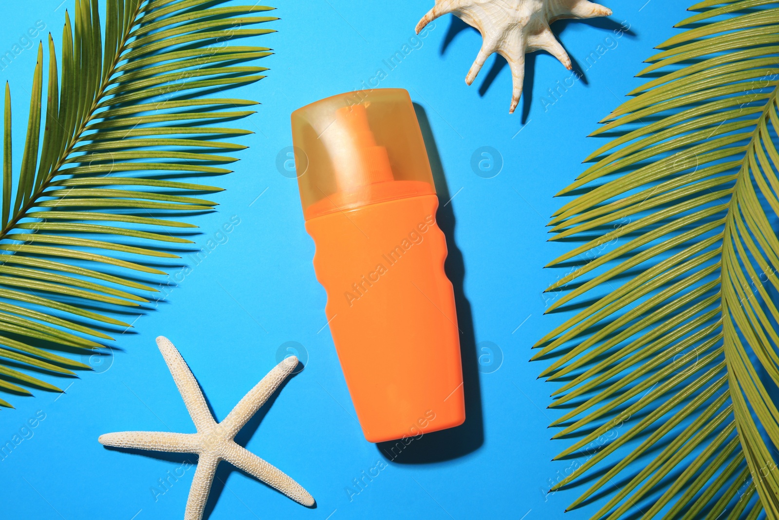 Photo of Flat lay composition with sunscreen and tropical leaves on light blue background. Sun protection care