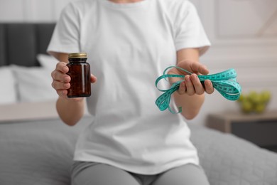 Photo of Woman with pills and measuring tape on bed in room, closeup. Weight loss