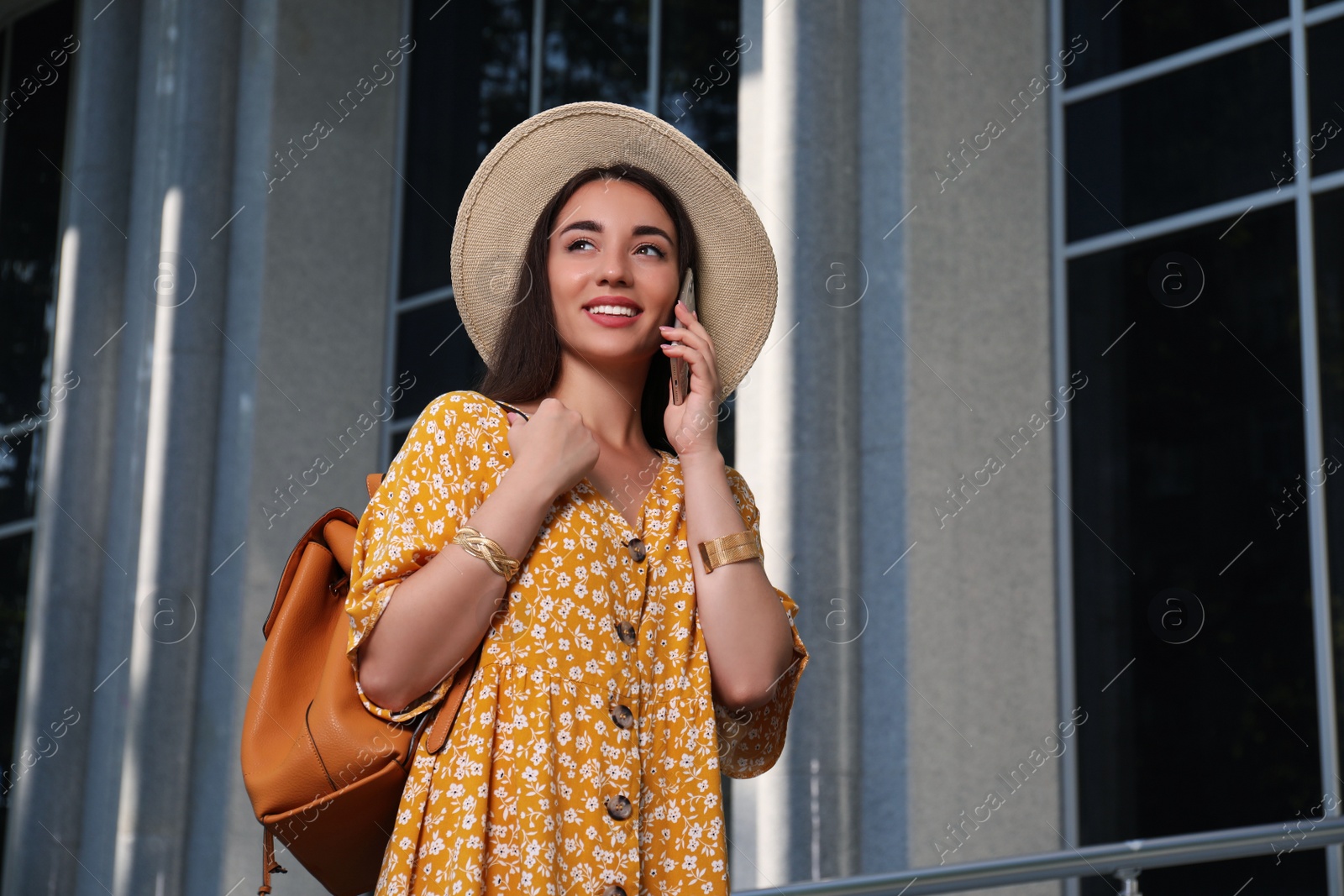 Photo of Beautiful young woman with stylish backpack talking on phone outdoors