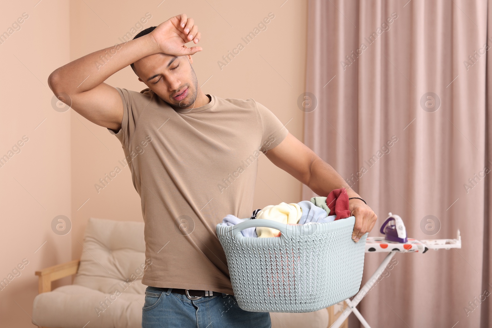 Photo of Tired man with basket full of laundry at home