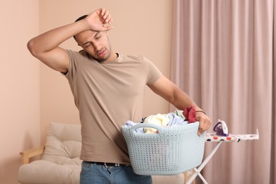 Photo of Tired man with basket full of laundry at home