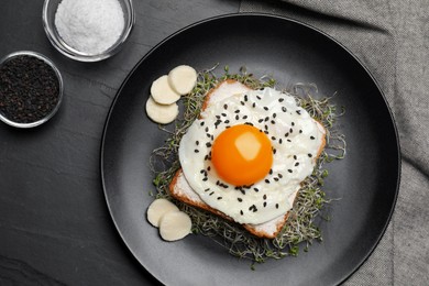 Photo of Tasty toast with egg, cheese and microgreens on black table, top view