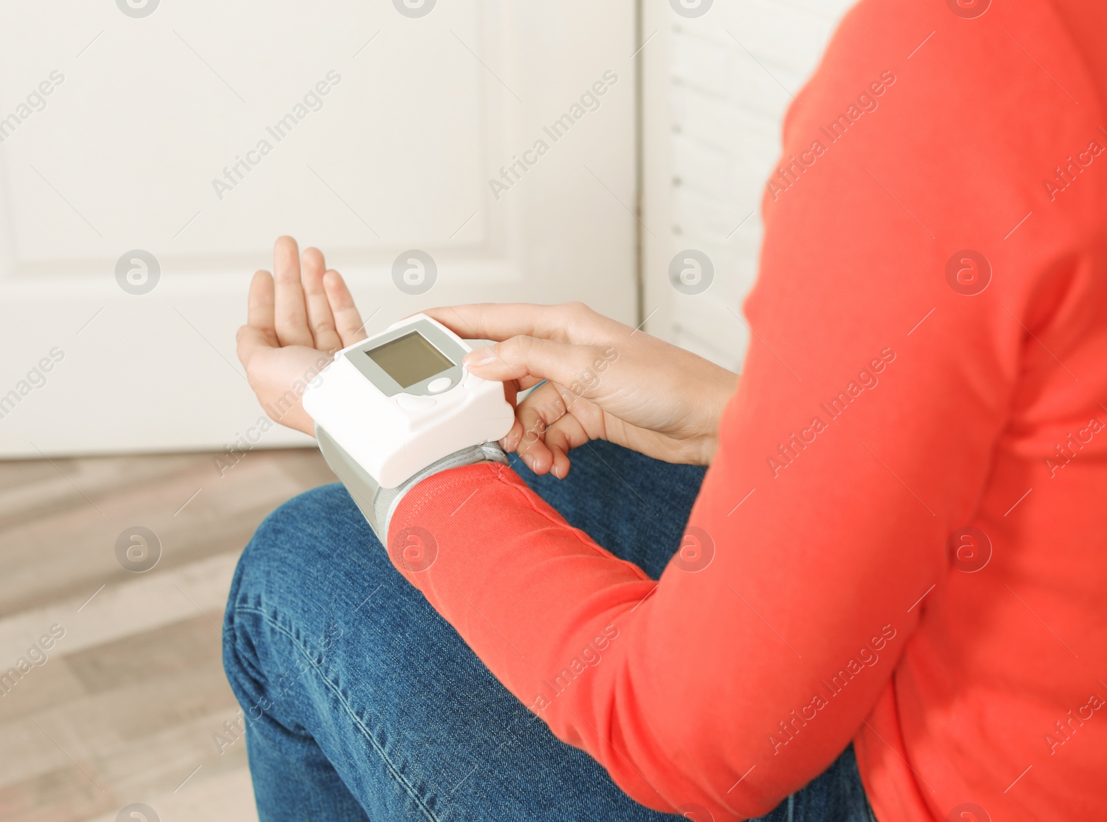 Photo of Young woman checking pulse with digital medical device indoors, closeup