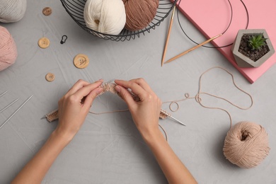 Woman knitting with threads at grey table, top view. Engaging hobby