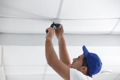 Technician installing CCTV camera on ceiling indoors