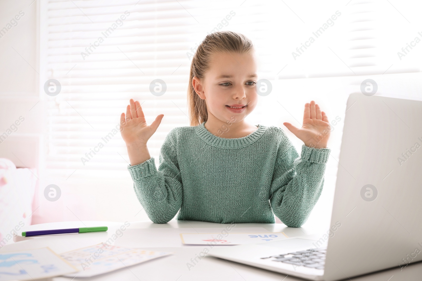 Photo of Little girl learning English indoors at online lesson