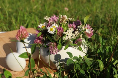 Photo of Ceramic mortar with pestle, different wildflowers and herbs on green grass outdoors