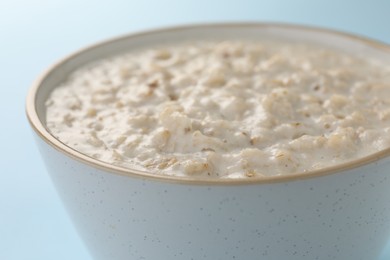 Photo of Tasty boiled oatmeal in bowl on light blue table, closeup