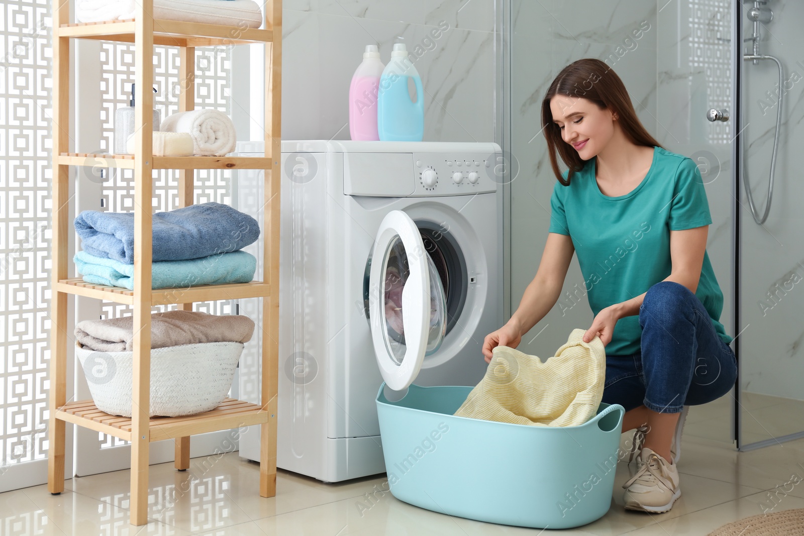 Photo of Young woman with clothes near washing machine in bathroom. Laundry day