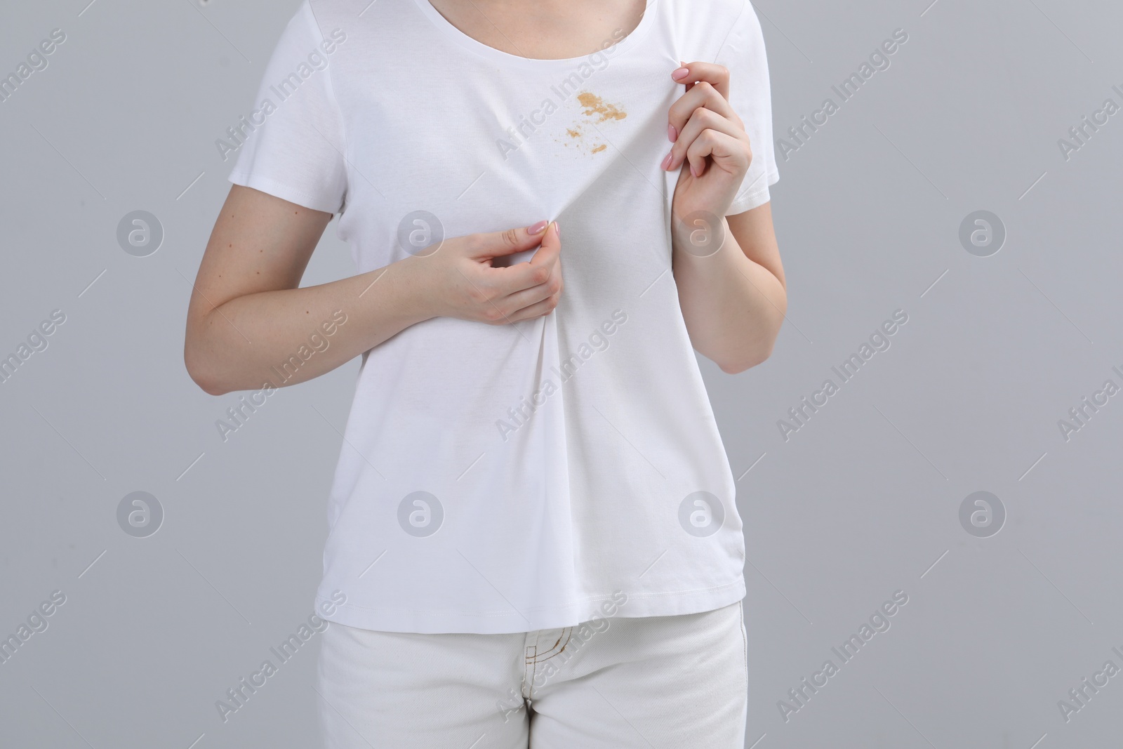 Photo of Woman showing stain on her t-shirt against light grey background, closeup