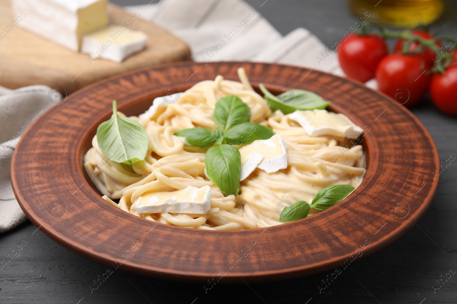 Photo of Delicious pasta with brie cheese and basil leaves on grey wooden table, closeup