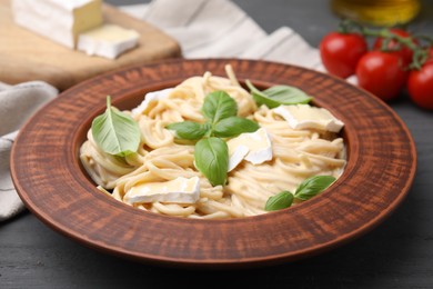 Delicious pasta with brie cheese and basil leaves on grey wooden table, closeup