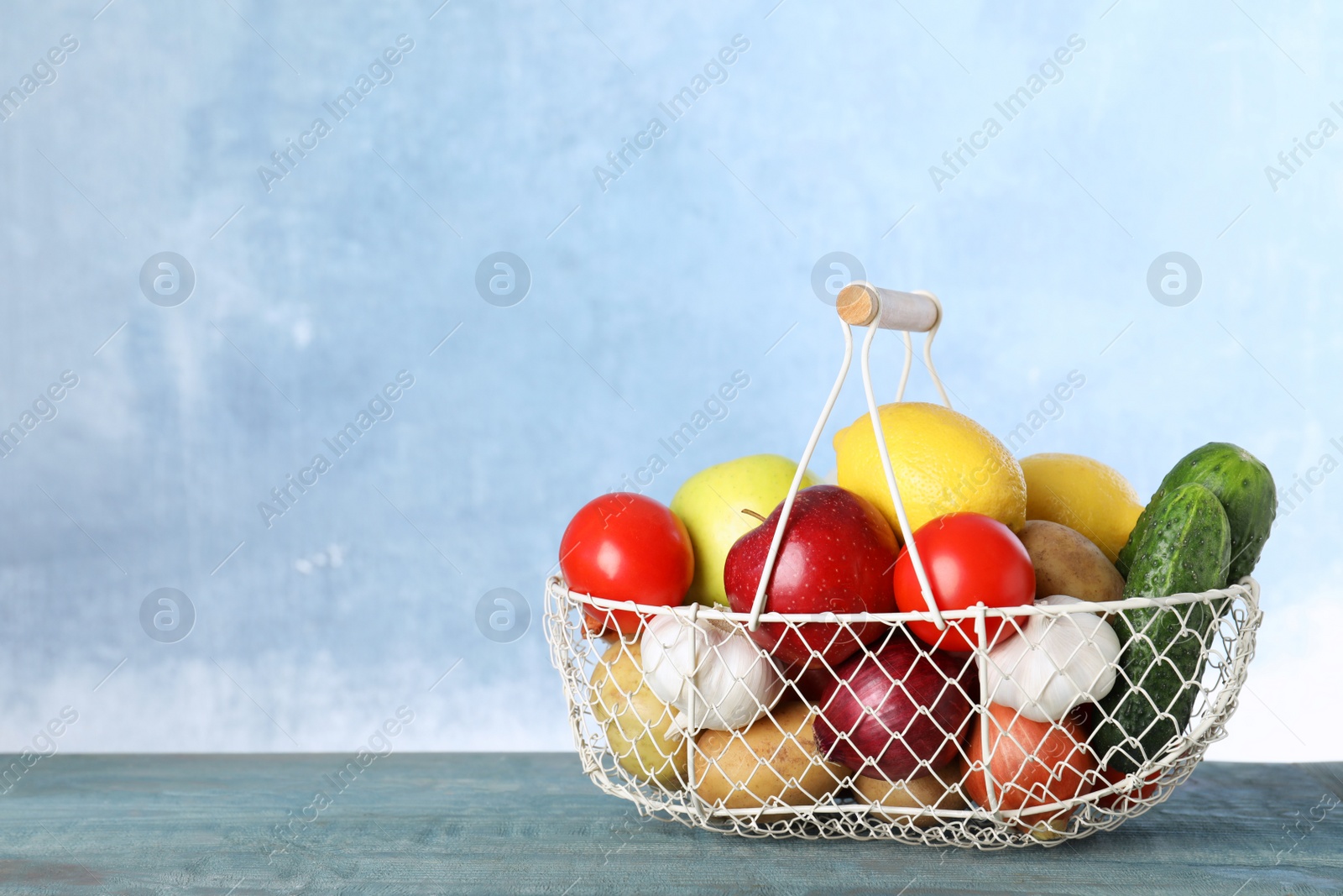 Photo of Basket full of fresh vegetables and fruits on table against color background, space for text