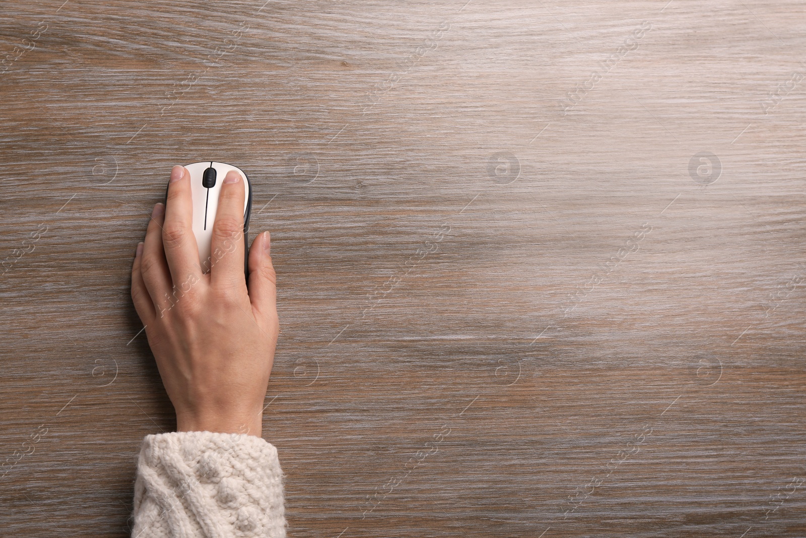 Photo of Woman using computer mouse on wooden table, top view. Space for text