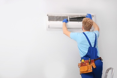 Photo of Professional technician maintaining modern air conditioner indoors