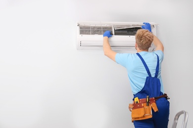 Professional technician maintaining modern air conditioner indoors