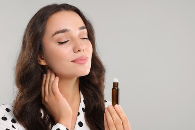 Photo of Beautiful young woman with roller bottle of essential oil on light grey background, space for text