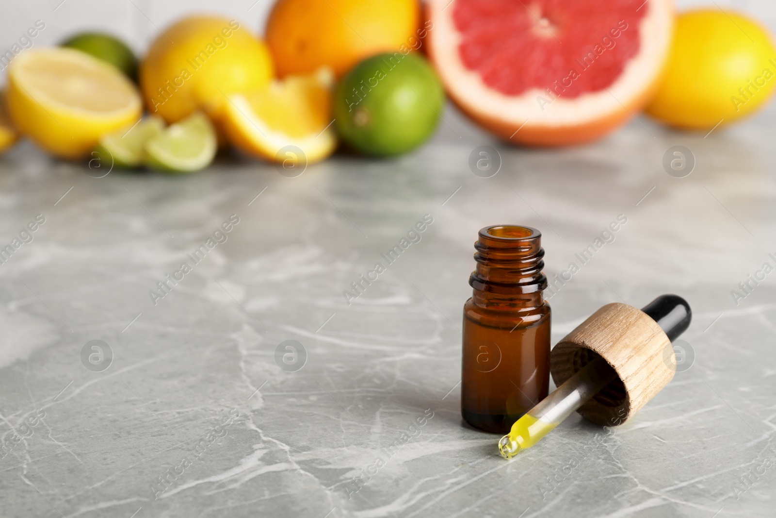 Photo of Bottle of essential oils with different citrus fruits on grey marble table. Space for text