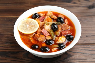 Meat solyanka soup with sausages, olives and vegetables on wooden table, closeup