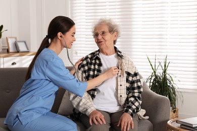 Photo of Young caregiver examining senior woman on sofa in room. Home health care service